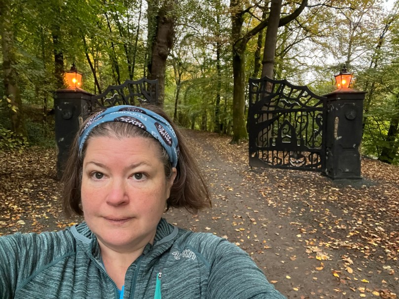 Selfie of my head and shoulders in front to ominous looking Halloween themed gates leading up a woodland path
